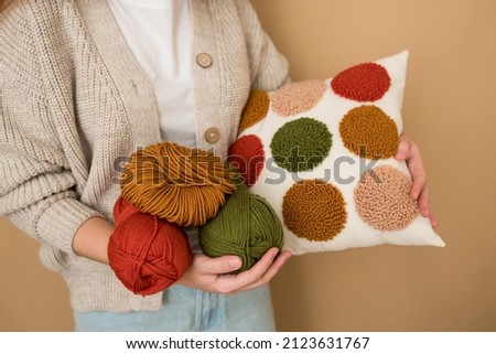 Punch needle embroidery pillow diy. Close-up of woman hands holding pillow. Product is made according to the technique pushing woolen threads on foundation fabric with needle with wood handle Royalty-Free Stock Photo #2123631767