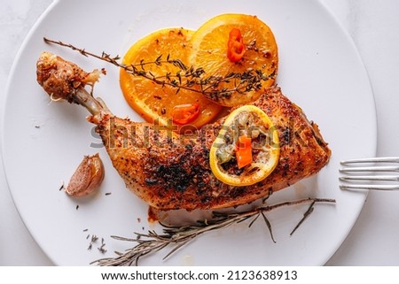 roasted fried turkey duck thighs, rubbed with spices and salt, on a baking sheet, with oranges, lemons, garlic, rosemary, thyme and olive oil. the concept of a healthy and tasty dinner for two.