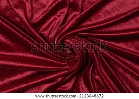 Swirled red-colored fabric texture background. This velvet fabric is made of 100% polyester.