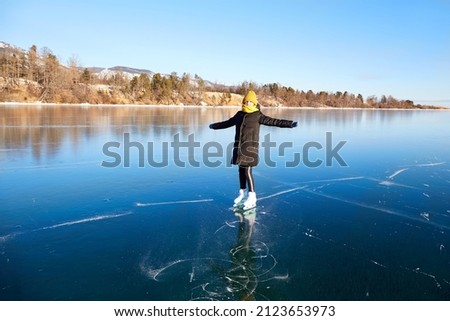 A young happy girl is skating on the transparent ice of the frozen Lake Baikal on a sunny winter day. Transparent ice, natural background. The concept of active winter recreation and sports. 