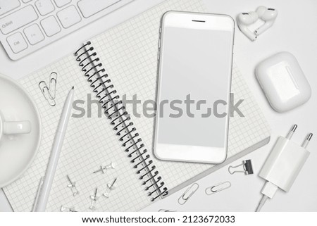 top view of office desk workspace with smartphone blank screen and empty notebook, coffee cup, headphones, charger, gadgets, keyboard on white background with copy space. Creative Designer concept.
