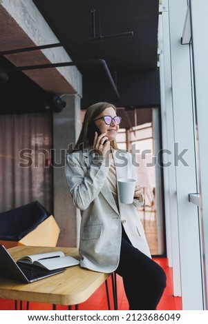 Successful young woman solving business problems during a telephone conversation, sitting in a modern cafe and working with a laptop. Cute interior is enjoying his free time in the cafe.