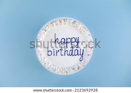 white cake with the inscription happy birthday on blue background, top view.