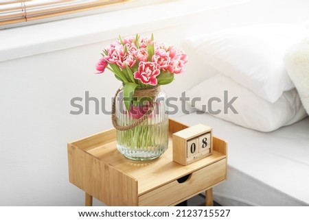 Bouquet of tulips and wooden cube calendar with date MARCH 8 on bedside table. International Women's Day celebration