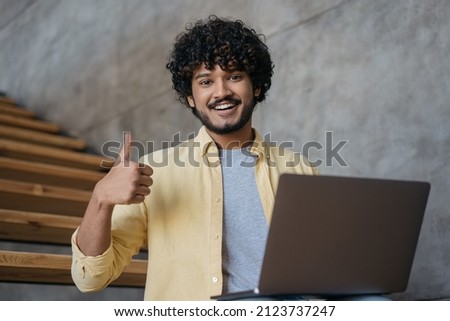 Smiling Indian man freelancer using laptop computer showing thumb up  looking at camera working online from home.  Asian student studying, watching training courses, online education concept 