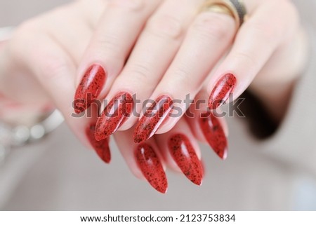 Female hand with long nails and a bright red manicure holds a bottle of nail polish