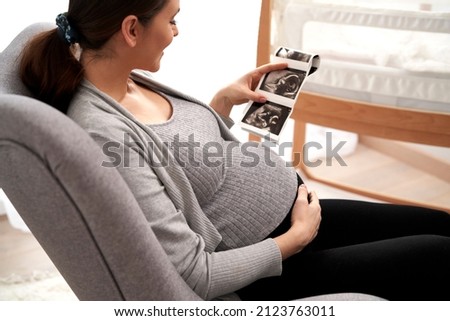 Caucasian woman in advanced pregnancy browsing ultrasound scan in baby's room Royalty-Free Stock Photo #2123763011