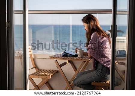 A young woman is drawing on digital tablet on the terrace near the sea