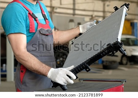 Spare parts for the car. The engine cooling radiator is in the hands of an auto mechanic. Inspection of the radiator before installation. Car repair in a car service. Royalty-Free Stock Photo #2123781899