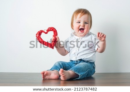 Handsome blonde toddler in shirt and garland of hearts for February 14th. Congratulations from little man.