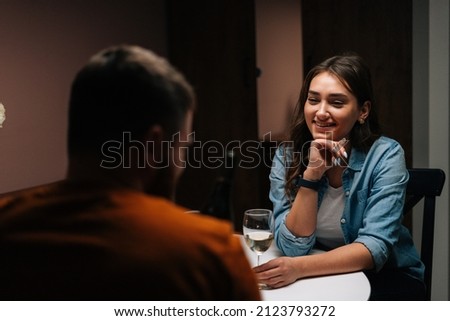 Back view of happy young couple enjoying talking and sitting together at dinner table with candles in cozy dark room. Love couple celebrating anniversary or Valentines day having romantic dinner