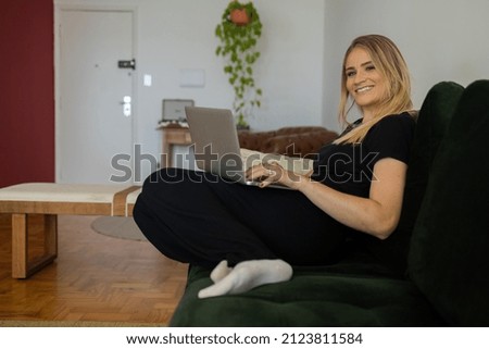Young woman working at home from her living room couch with laptop on her lap. Home office concept. Gray notebook for working. Home office concept. High quality photo