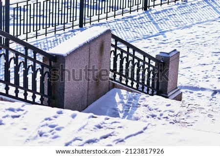 A fragment of the snow-covered city embankment of the Amur River. Winter morning. Metal and granite. Staircase with a fence. Traces of people and animals on a white snow carpet.