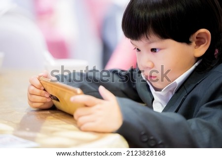 Asian boy watching cartoons with his smartphone. A 3 year old child wears black suit. Concept of baby use of digital media in long time.