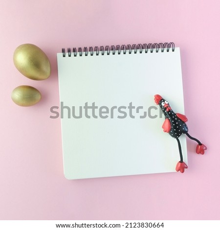 Golden Easter eggs, an open notebook and a figurine of a black chicken on a pink pastel background. Easter template, minimalistic design. Top view, flat lay, copy space.
