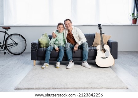 Smiling man hugging preteen son near acoustic guitar at home