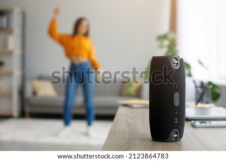 Millennial woman dancing to favorite music at home, selective focus on portable wireless speaker, free space. Young female moving to popular song, using modern stereo system indoors Royalty-Free Stock Photo #2123864783