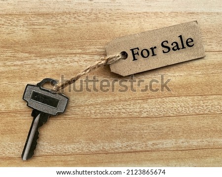 Text on brown tag with house key and wooden table background - For sale. Property concept.