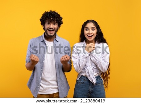 Wow, yes. Portrait of overjoyed indian man and woman cheering and shaking clenched fists, looking at camera in excitement. Happy couple celebrating win over yellow studio background wall