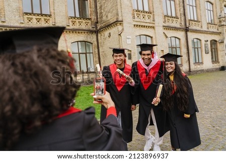 Graduate wearing gown and caps taking photo of her friends in university yard
