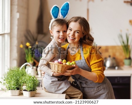 Sweet family portrait of happy mother and little son holding wicker basket full of painted multi-colored Easter eggs, tenderly embracing and smiling in cozy light kitchen at home, selective focus Royalty-Free Stock Photo #2123900627