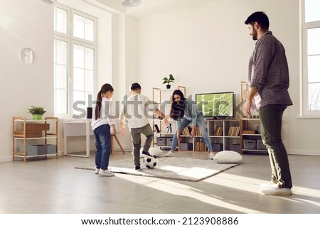 Happy family having fun at home. Kids playing soccer with mom and dad. Brother and sister playing football together with parents in big living room with large television set in new modern apartment Royalty-Free Stock Photo #2123908886
