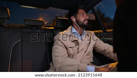 Young businessman listening music through earphones traveling on backseat in car. Cheerful man in headphones sing song relaxing on backseat of taxi cab Royalty-Free Stock Photo #2123915648