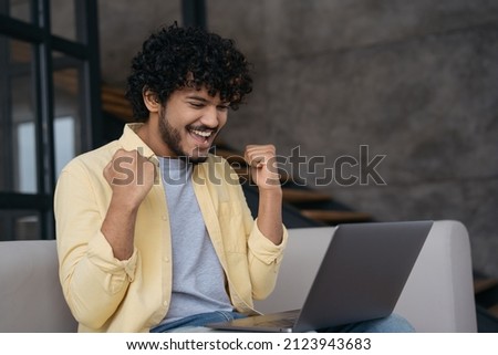 Excited Indian man watching football game, celebration victory sitting at home. Emotional guy win online sports betting  Royalty-Free Stock Photo #2123943683