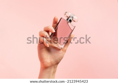 A template for perfume and toilet water. A woman's hand elegantly holds a glass perfume bottle on a pink background, close-up. Copy space. The concept of perfumery and beauty. Royalty-Free Stock Photo #2123945423