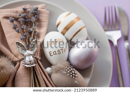 Banner. Table setting. A plate with a rabbit on a napkin, lavender and Easter eggs on a fashionable background of 2022 is a veri pery. Top view. The concept of a happy Easter holiday for cafes. Royalty-Free Stock Photo #2123950889