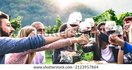 Happy friends enjoying harvest time together drinking at farm house countryside - Life style concept with millenial people hands toasting red wine glasses at vineyard - Horizontal crop filter
