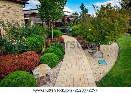Front yard, landscape design with multicolored shrubs intersecting with bright green lawns behind the house is a modern, garden care service, green grass with a beautiful yard for the background. Royalty-Free Stock Photo #2123972297