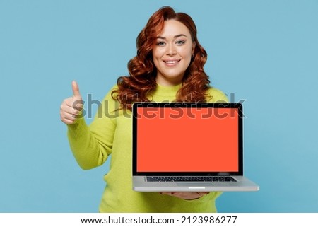 Young chubby overweight plus size big fat woman in green sweater hold use work laptop pc computer blank screen workspace area show thumb up isolated on plain blue background People lifestyle concept