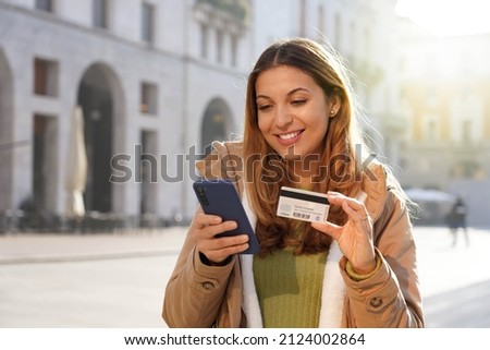 Close up of young woman typing number of credit card on smartphone makes purchase online or checks bank account outdoors