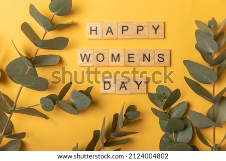 International Women's Day.Beautiful card for March 8.Bouquet of eucalyptus and text happy women's day on a yellow paper background. Holiday concept.Copy space.Top view. Royalty-Free Stock Photo #2124004802