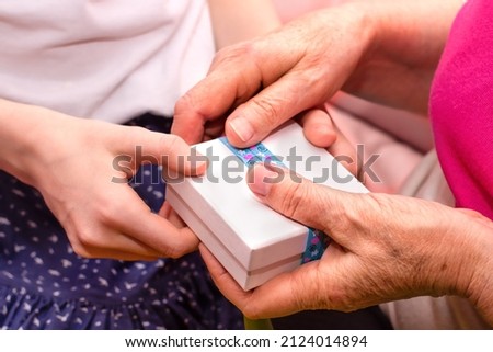 Young and elderly women's hands hold a gift box
