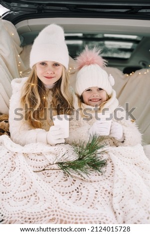 Two little girls in the winter forest. Two sisters hugging. Rest in the winter forest. Girls dressed in white warm clothes. Christmas vacation.