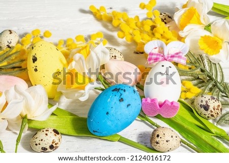Spring Easter festive background with pastel eggs, cute bunnies, and traditional spring flowers. Hard light, dark shadow, white wooden background, close up
