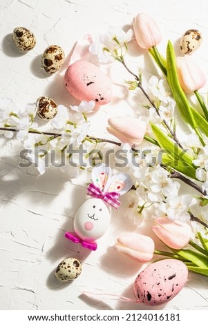 Happy Easter background with blooming cherry, tulips and cute rabbit. Spring festive flat lay, traditional symbols, hard light dark shadow, white putty background, close up
