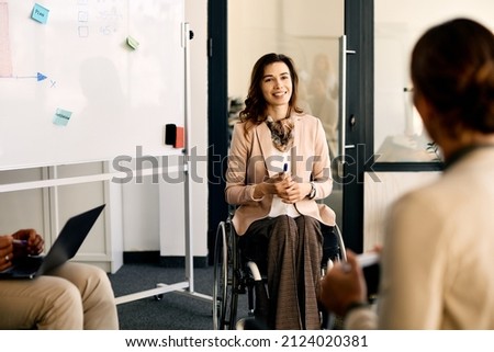 Happy businesswoman with disability sitting in wheelchair while brainstorming with her coworker during presentation in meeting room. Royalty-Free Stock Photo #2124020381
