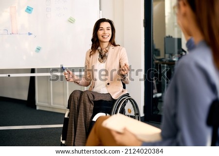 Happy CEO in wheelchair explaining inclusive business strategy to her coworkers during presentation in meeting room. Royalty-Free Stock Photo #2124020384