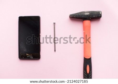Hammer, nail and mobile phone with broken display on pink background. Crashed smartphone concept. Top view.