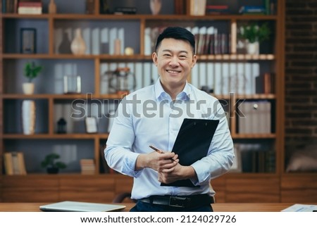 Portrait of a successful Asian teacher, a man in a shirt looking at the camera and smiling, in the classic office of the university director Royalty-Free Stock Photo #2124029726