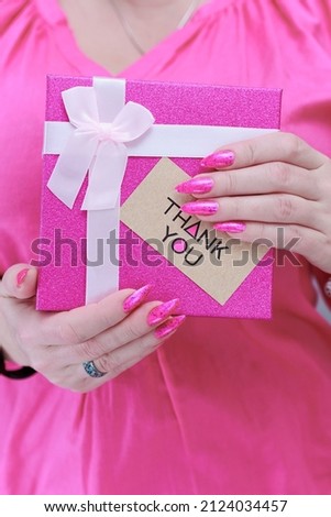 Female hands with long nails and neon pink nail polish hold a picture with the inscription Thank you