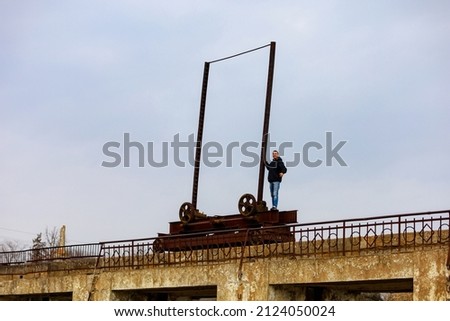 A young man or an adult guy a tourist or a hiker in a windbreaker looks into the distance while standing on the old power plant mechanism. Background with copy space for text.