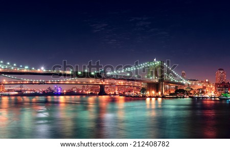 Brooklyn Bridge panorama over East River at night in New York City Manhattan with lights and reflections.