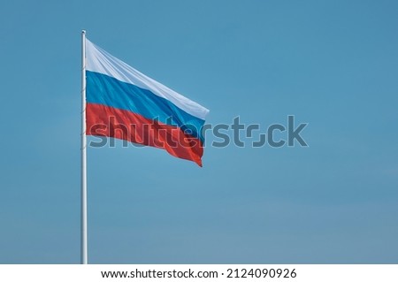 Flag of Russia against the blue sky. High flagpole on the embankment of the city of Blagoveshchensk, Russia. The tricolor cloth moves smoothly in the wind. Room for text.