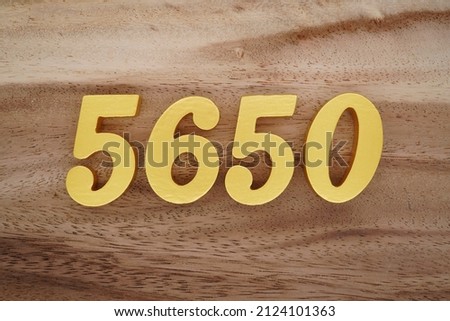 Wooden Arabic numerals 5650 painted in gold on a dark brown and white patterned plank background