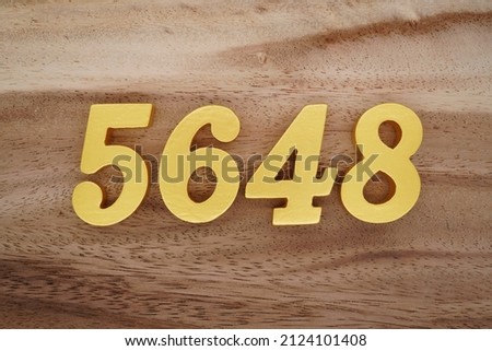 Wooden Arabic numerals 5648 painted in gold on a dark brown and white patterned plank background