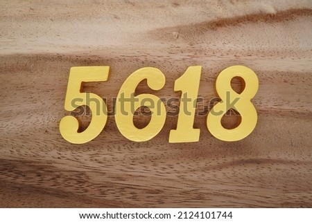 Wooden Arabic numerals 5618 painted in gold on a dark brown and white patterned plank background